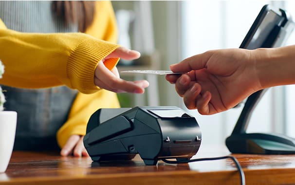 A person hands their debit card to a sales person at a counter. hey are near a payment system