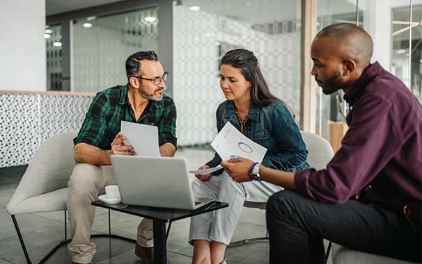 A man and woman are seated in front of a computer, and they appear to be meeting with a financial advisor