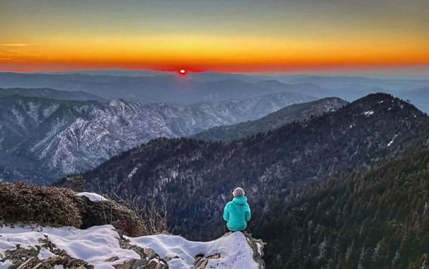 A photo of a person outside standing on a mountain, taking in the beautiful view