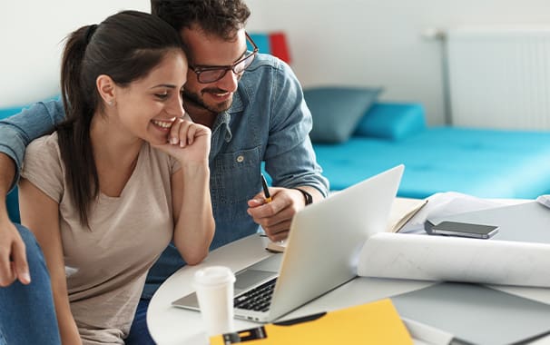 A man and a woman seated at a laptop computer are leaning in close to each other and looking at the screen